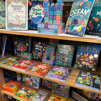 Bookstore shelf filled with colorful children's books and activity sets. Titles include "Ocean Adventure" and "Bird Watch," creating a playful, educational ambiance.