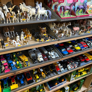 Shelves filled with toy animals and vehicles. Top shelves display horses and farm animals, while lower shelves hold colorful toy cars and machinery.