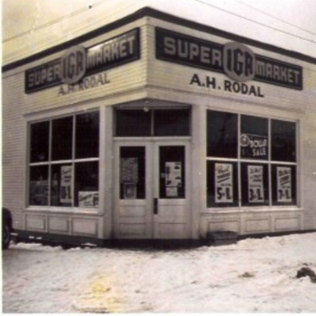 Vintage black-and-white photo of a Super IGA Market storefront named A.H. Rodal, with sale signs on snowy ground, conveying a nostalgic feel.