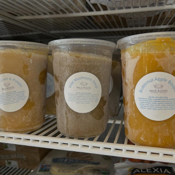 Three labeled containers of frozen soup are on a refrigerator shelf. Flavors include Leek & Potato, Wild Mushroom, and Butternut Apple Bisque.