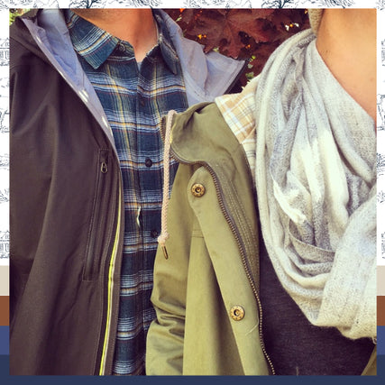 Clothing & BootsA couple wearing fall jackets stand shoulder to shoulder. The person on the left dons a plaid shirt under a dark coat, while the right wears a green jacket and scarf.