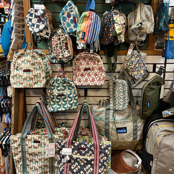 A display of colorful bags and backpacks with various patterns, including animals, stripes, and geometric designs, hangs on a store wall.