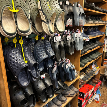 Display of assorted clogs and sandals in various colors on wooden shelves in a store. The atmosphere is casual and inviting for shoppers.
