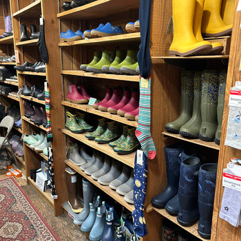 A vibrant display of colorful boots on wooden shelves, featuring yellow, green, and pink hues with patterned socks hanging nearby. Cozy and inviting atmosphere.
