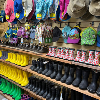 A store shelf displays a variety of colorful hats, flip-flops, and rain boots. Bright pink and red designs stand out, creating a cheerful, vibrant scene.